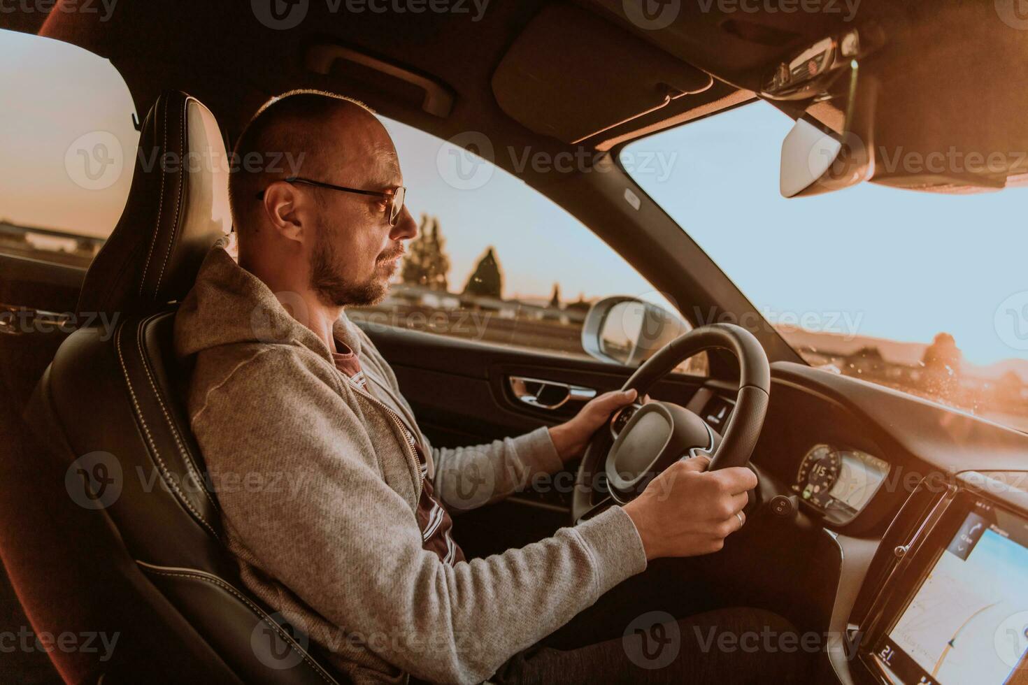 un hombre con un Gafas de sol conducción un coche a puesta de sol. el concepto de coche viaje foto