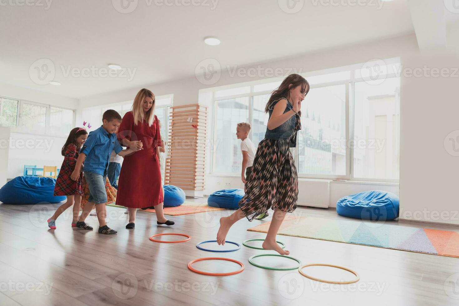 Small nursery school children with female teacher on floor indoors in classroom, doing exercise. Jumping over hula hoop circles track on the floor. photo