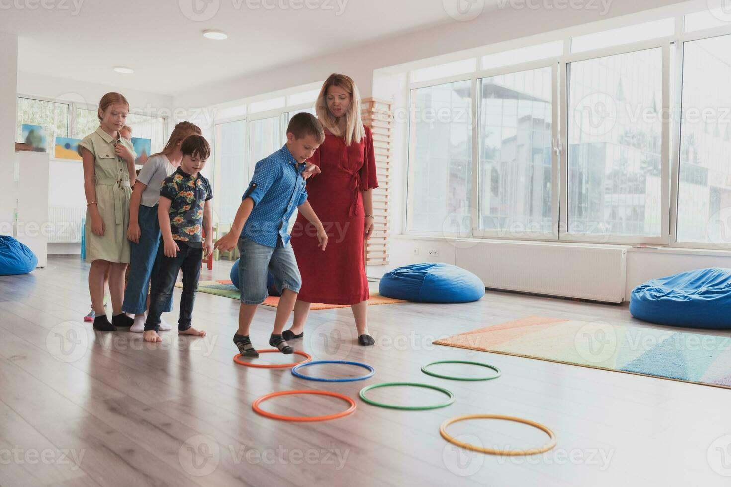 Small nursery school children with female teacher on floor indoors in classroom, doing exercise. Jumping over hula hoop circles track on the floor. photo