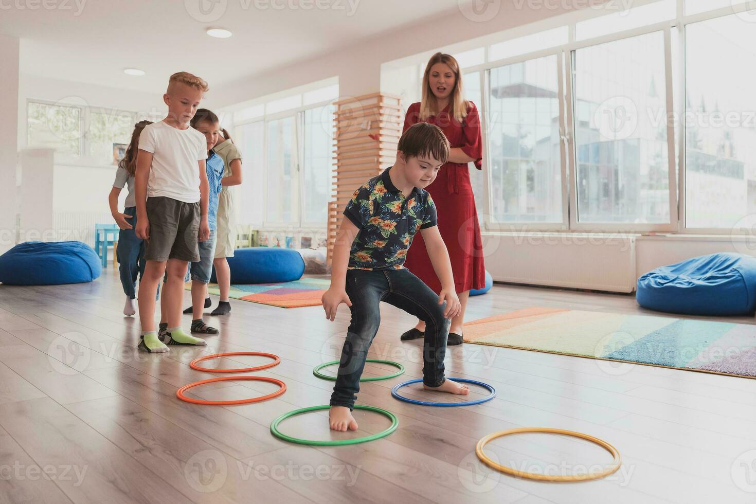 Small nursery school children with female teacher on floor indoors in classroom, doing exercise. Jumping over hula hoop circles track on the floor. photo