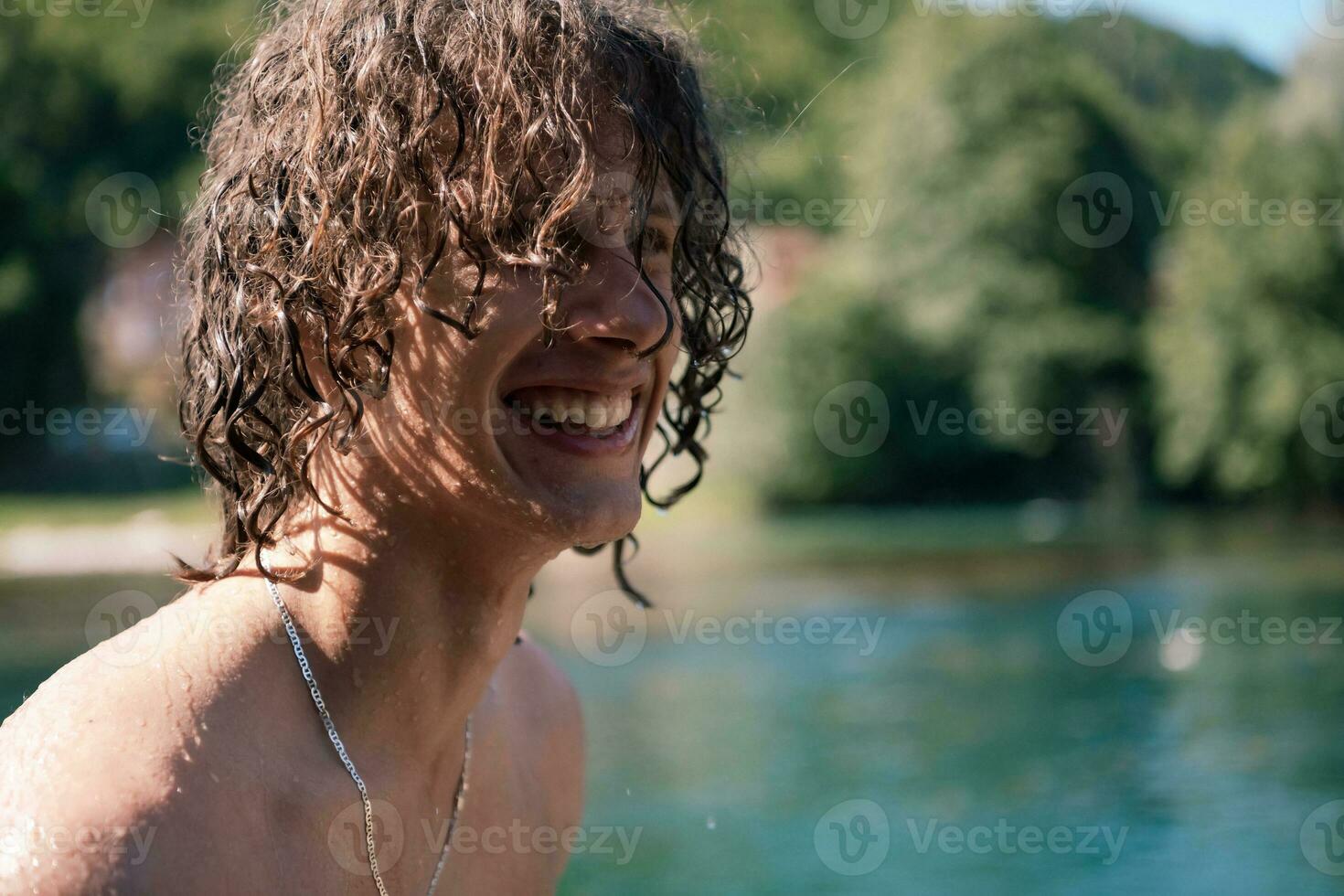 Portrait of a young teen boy with curly wet hair near the river having fun with friends at a summer party. photo