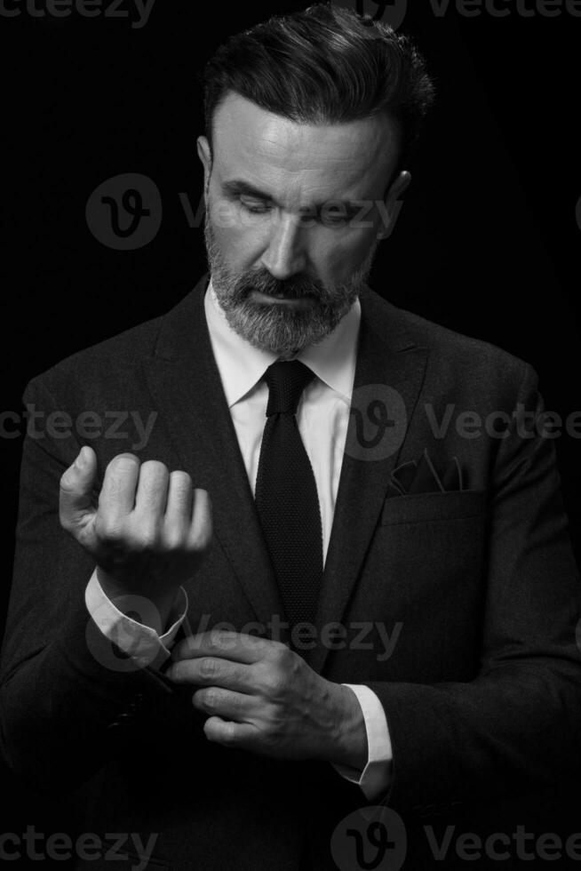 Portrait of a stylish elegant senior businessman with a beard and casual business clothes in photo studio adjusting suit