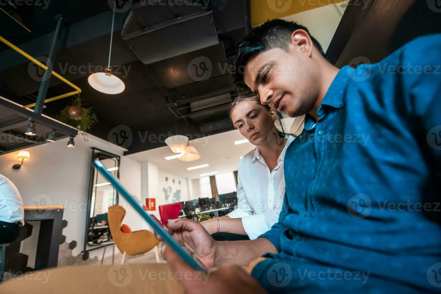 Multiethnic business people man with a female colleague working together on tablet computer in relaxation area of modern startup office photo