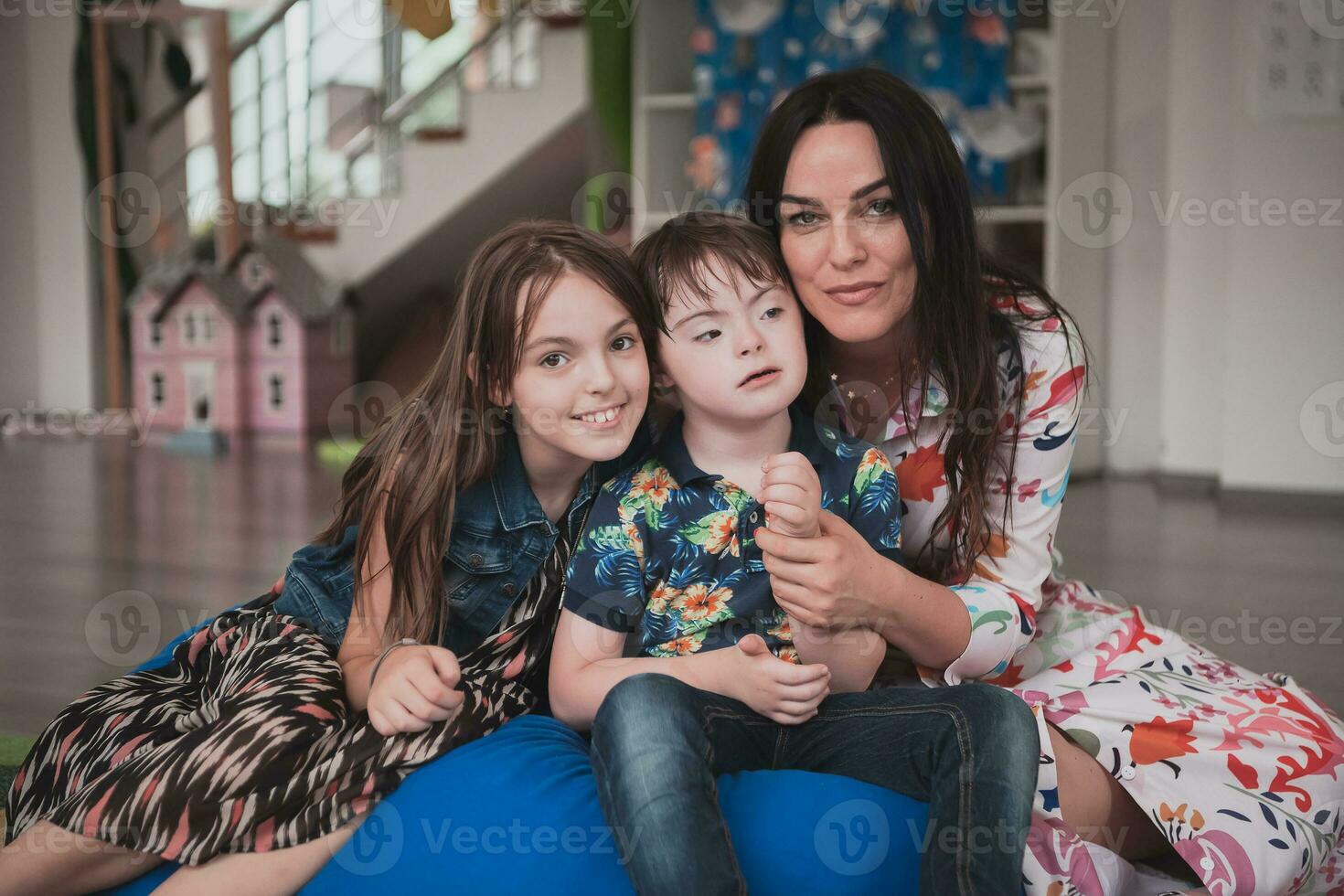 A girl and a woman hug a child with down syndrome in a modern preschool institution photo