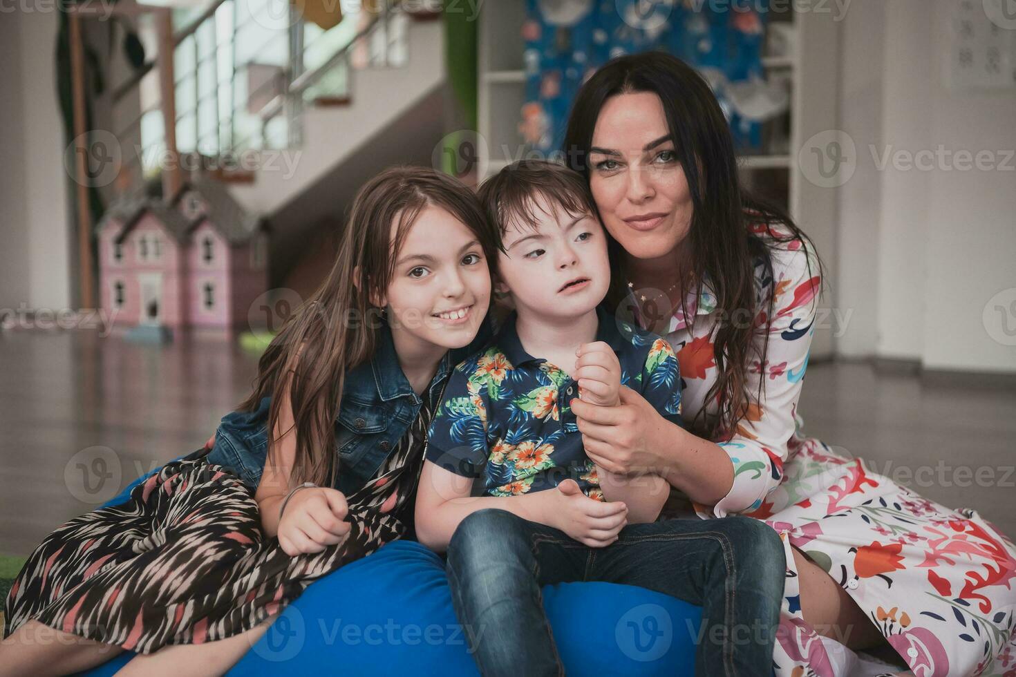 un niña y un mujer abrazo un niño con abajo síndrome en un moderno preescolar institución foto