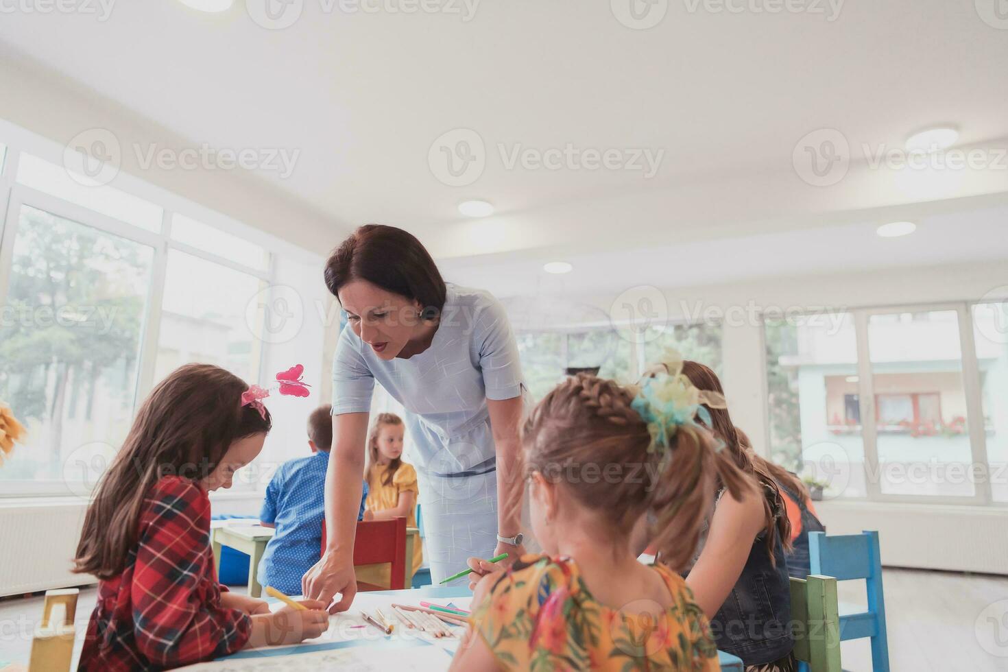 Creative kids during an art class in a daycare center or elementary school classroom drawing with female teacher. photo