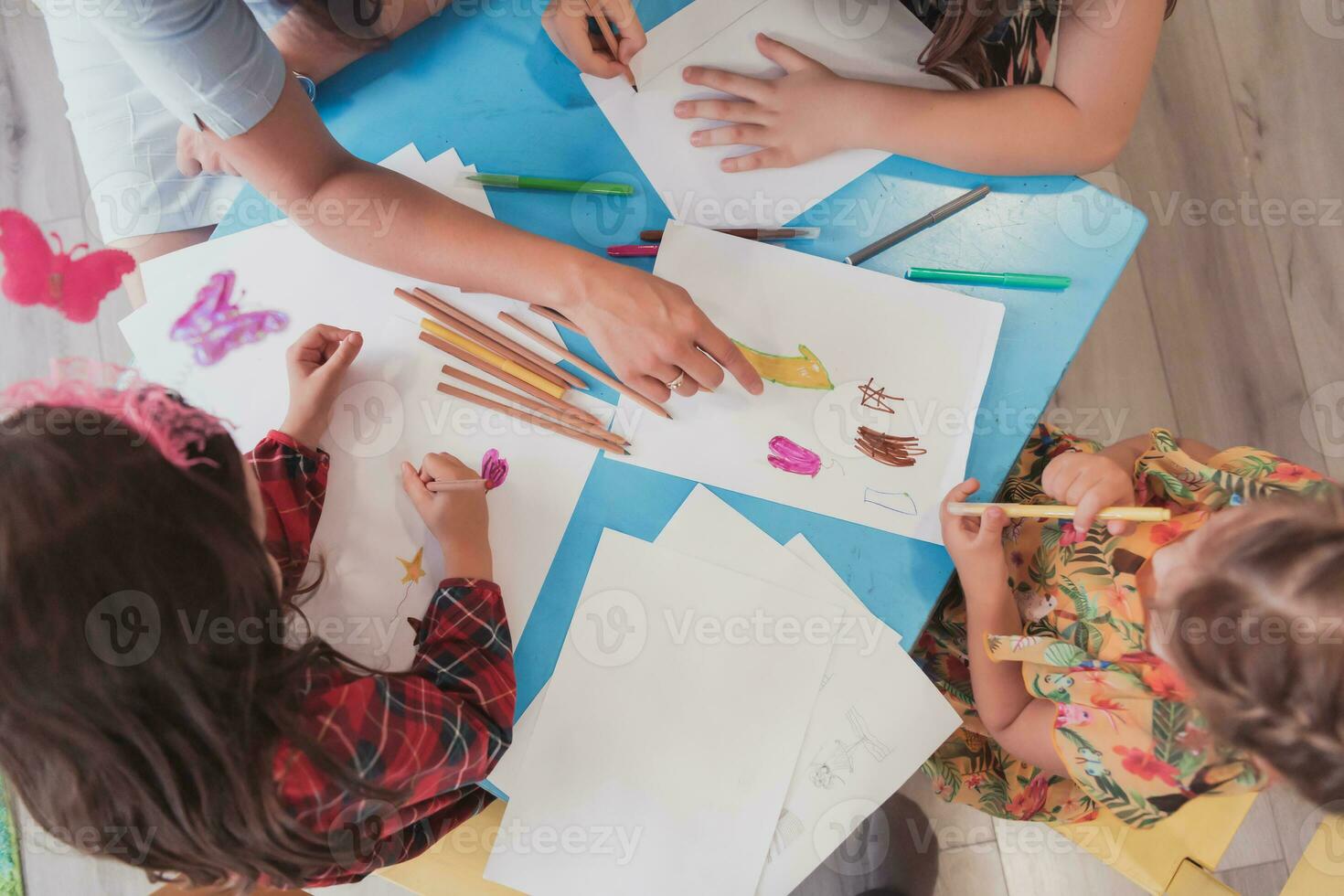 Creative kids during an art class in a daycare center or elementary school classroom drawing with female teacher. photo