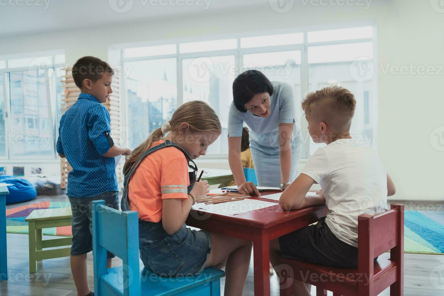 Creative kids during an art class in a daycare center or elementary school classroom drawing with female teacher. photo
