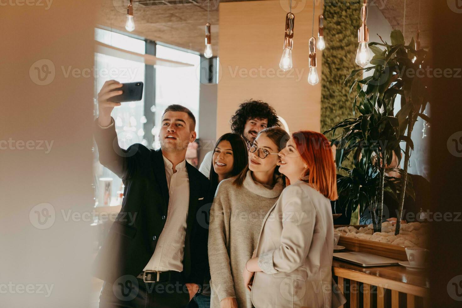 grupo de colegas alegres tomando selfie y gesticulando mientras están de pie en la oficina moderna. foto