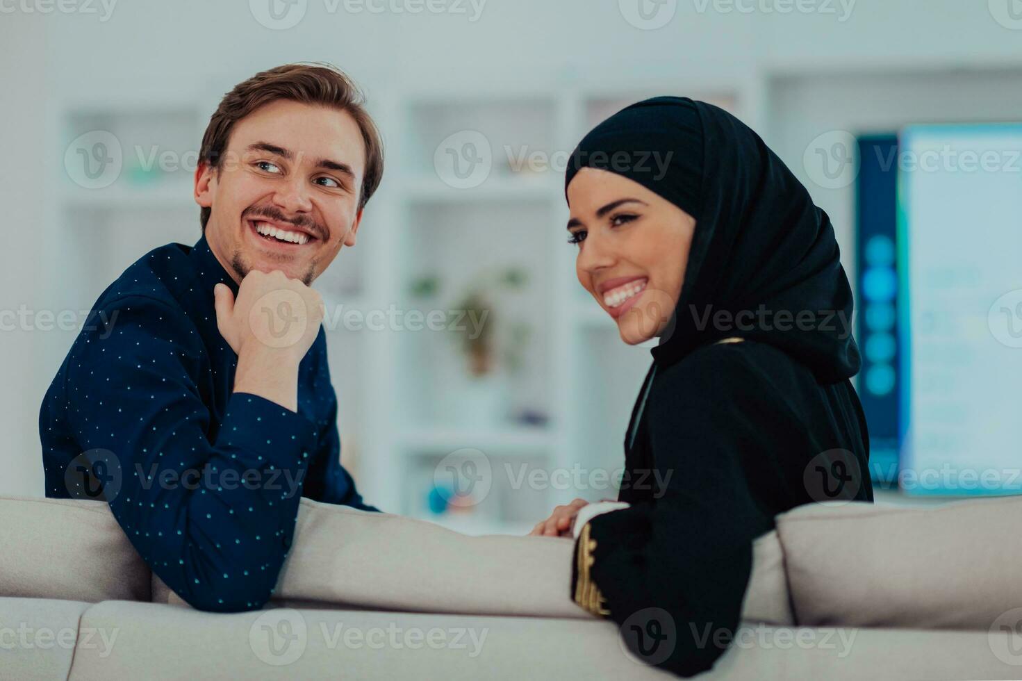 Young muslim couple woman wearing islamic hijab clothes sitting on sofa watching TV together during the month of Ramadan at modern home photo