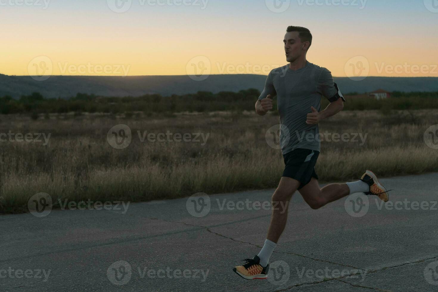 Attractive fit man running fast along countryside road at sunset light, doing jogging workout outdoors photo