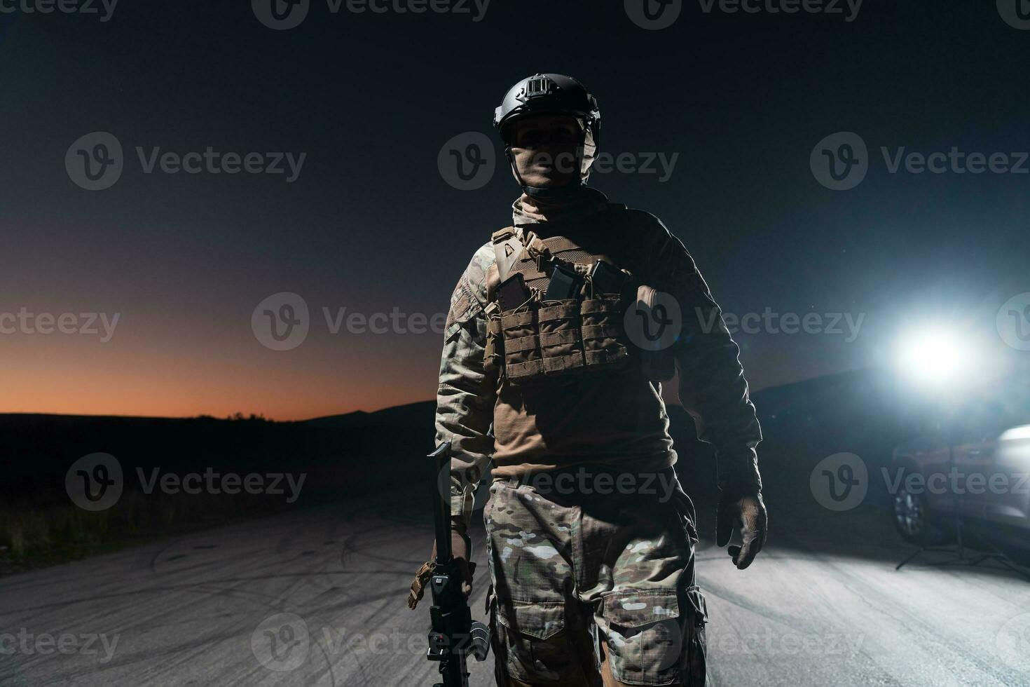 Army soldier in Combat Uniforms with an assault rifle, plate carrier and combat helmet going on a dangerous mission on a rainy night. photo