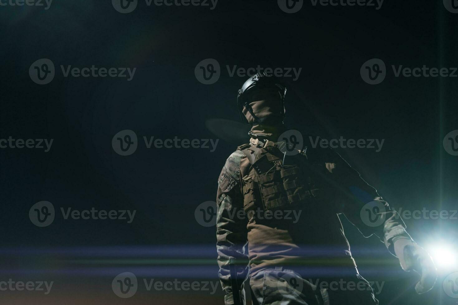 Army soldier in Combat Uniforms with an assault rifle, plate carrier and combat helmet going on a dangerous mission on a rainy night. photo
