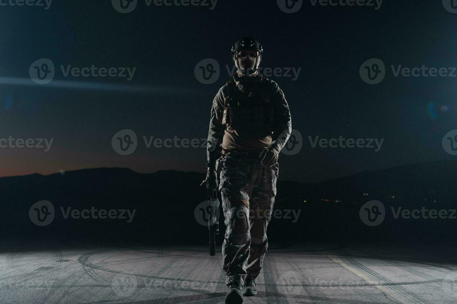 Army soldier in Combat Uniforms with an assault rifle, plate carrier and combat helmet going on a dangerous mission on a rainy night. photo