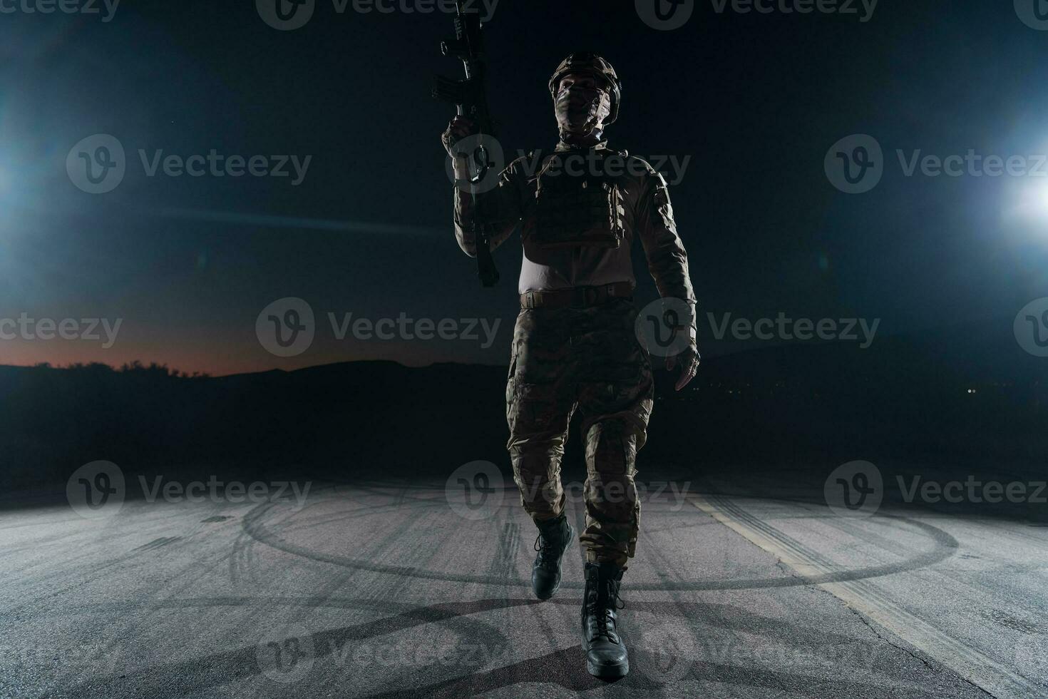 Army soldier in Combat Uniforms with an assault rifle, plate carrier and combat helmet going on a dangerous mission on a rainy night. photo