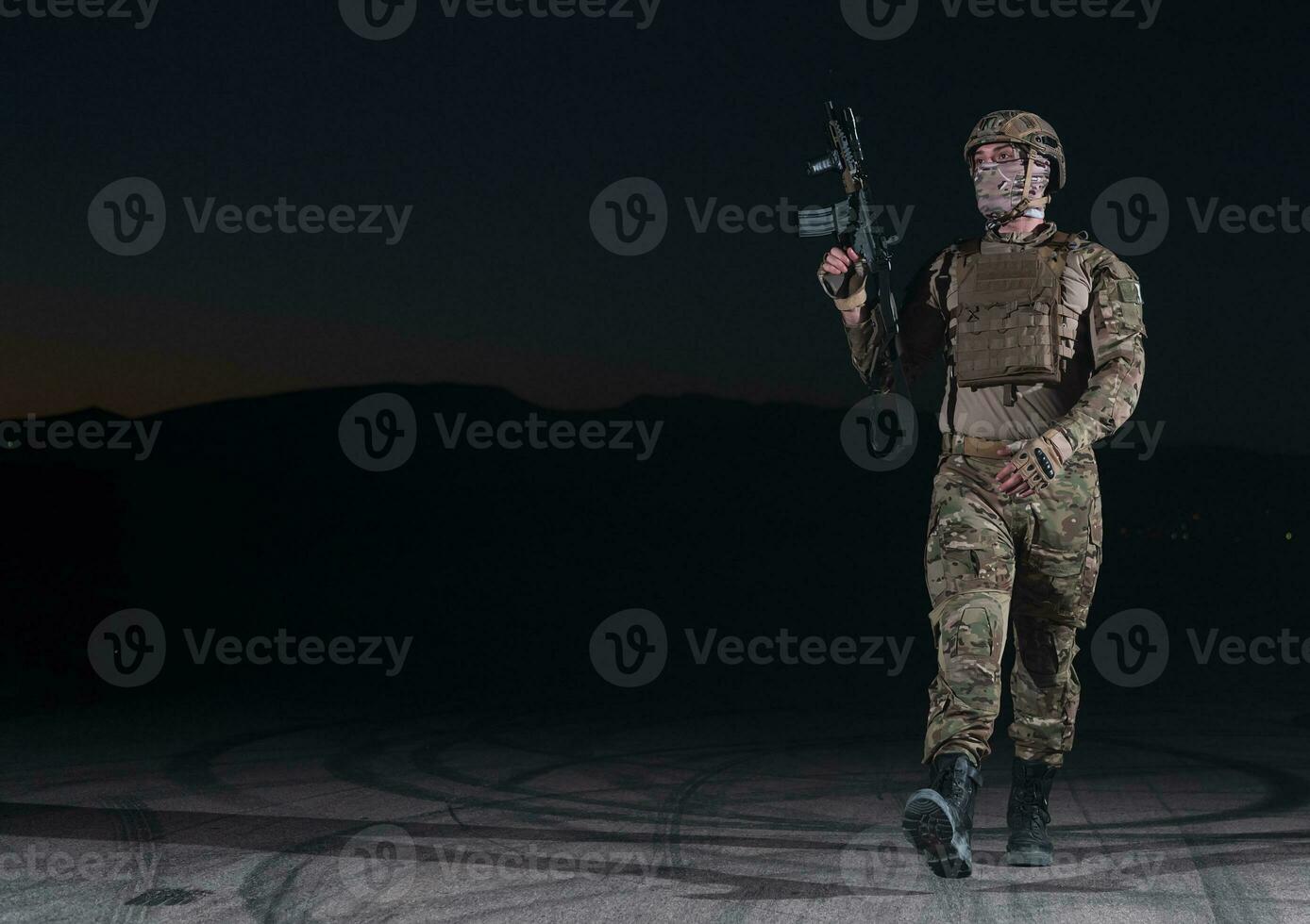 Army soldier in Combat Uniforms with an assault rifle, plate carrier and combat helmet going on a dangerous mission on a rainy night. photo