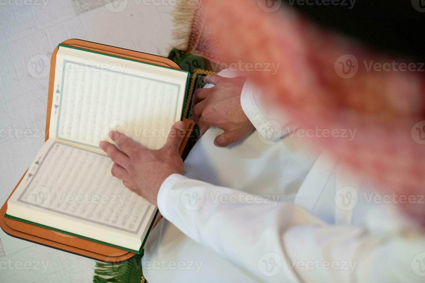 Young arabian muslim man in traditional clothes reading holy book Quran on the praying carpet before iftar dinner during a ramadan feast at home photo