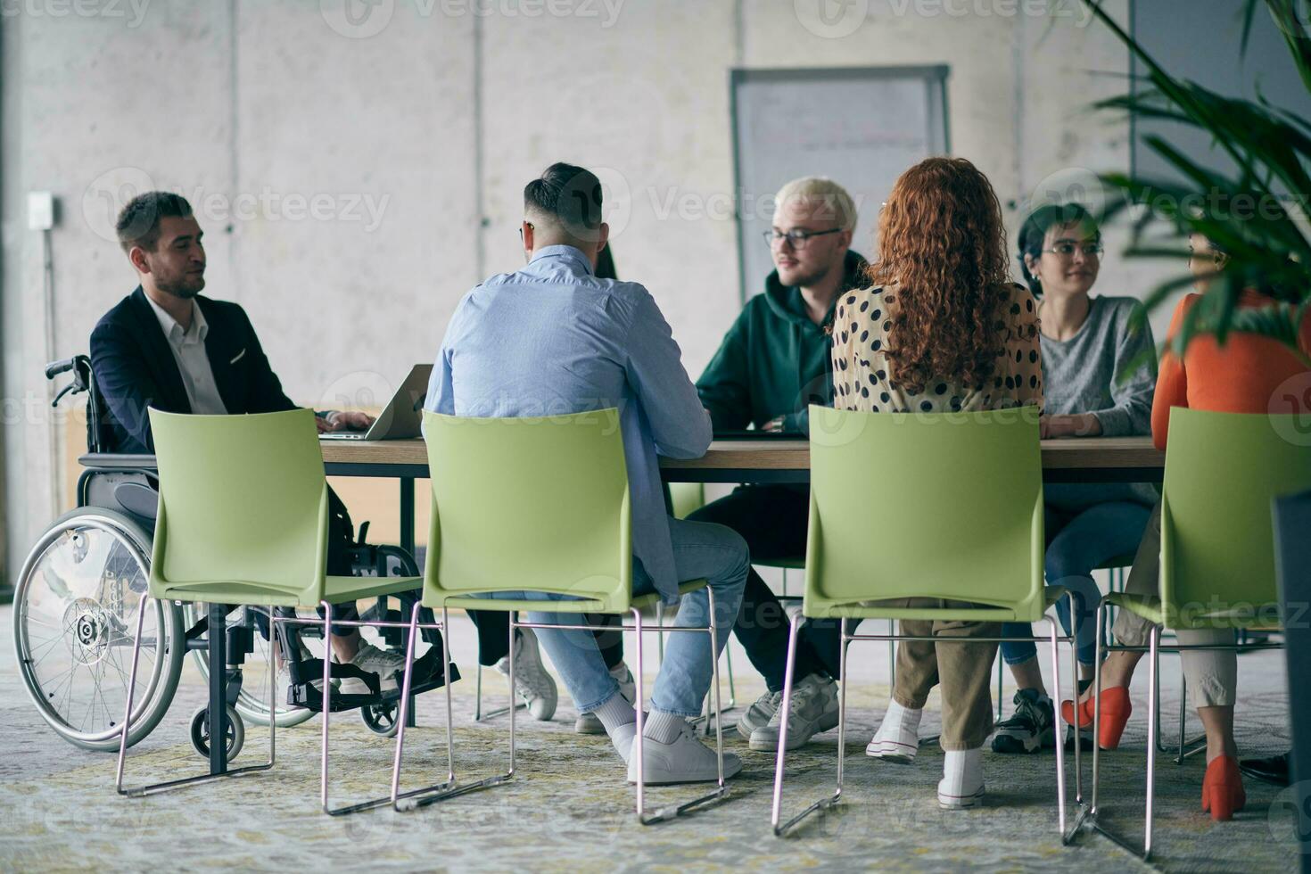 A diverse group of business professionals, including an person with a disability, gathered at a modern office for a productive and inclusive meeting. photo