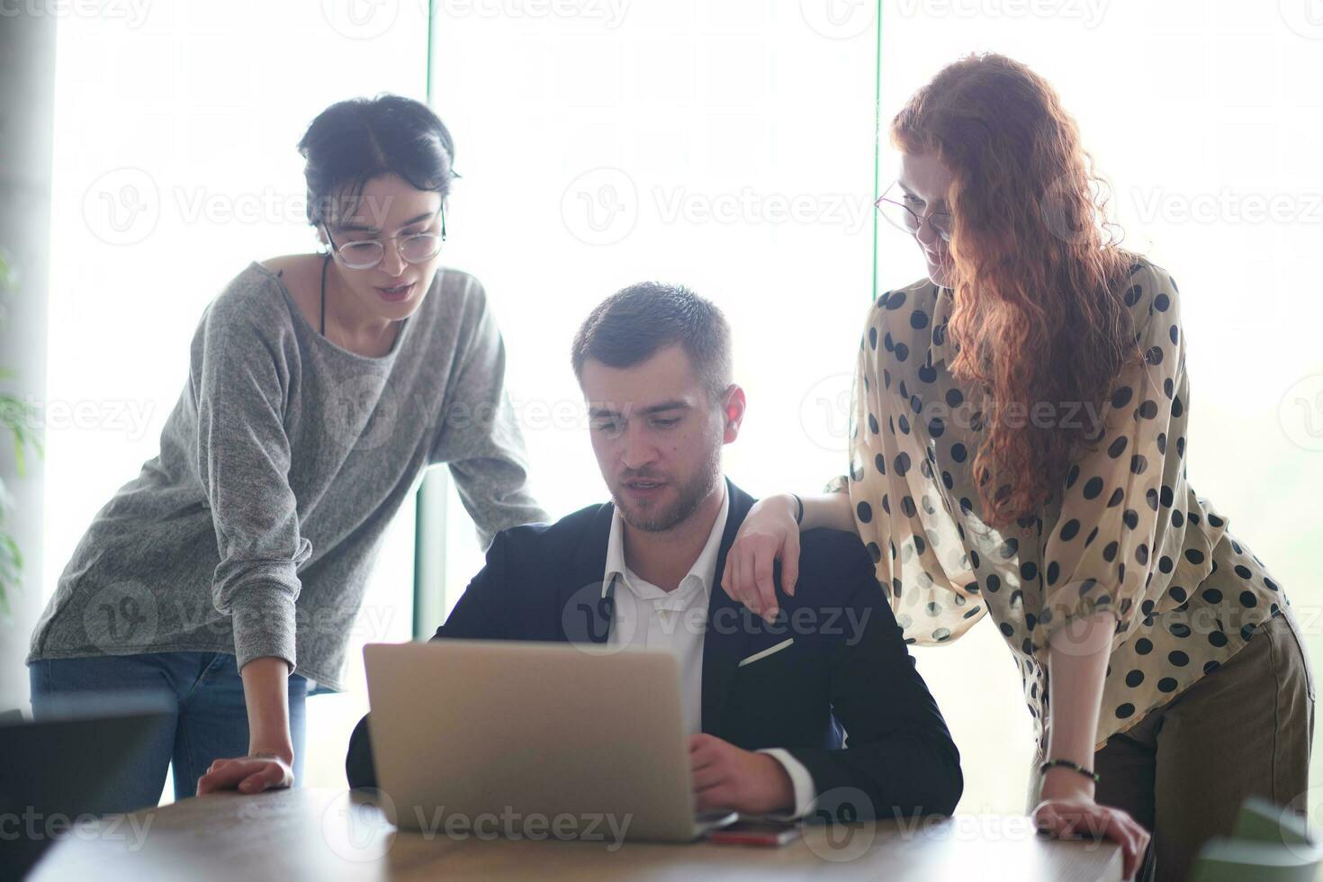 A businessman engaging in a discussion about sales statistics with his two female colleagues while they examine the data on a laptop in a modern office setting photo