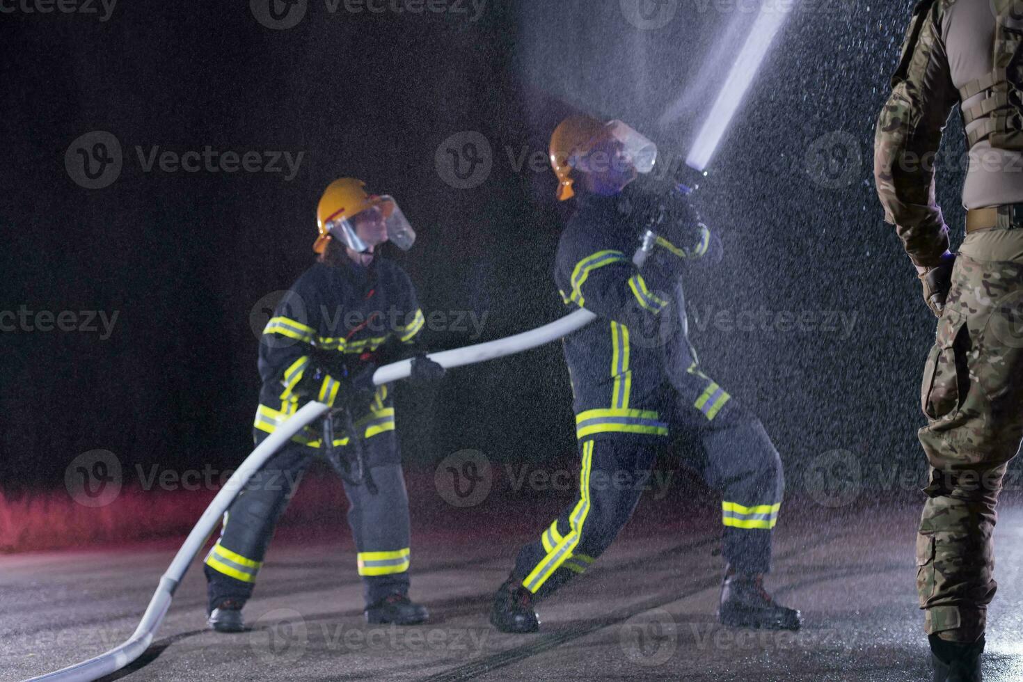 Firefighters using a water hose to eliminate a fire hazard. Team of female and male firemen in dangerous rescue mission. photo