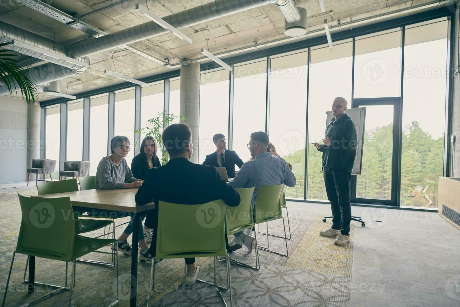 In a modern office setting, a group of business professionals attentively listens to a captivating presentation delivered by their young colleagues, showcasing their teamwork, engagement, and eagerness to learn and grow in a collaborative environment. photo