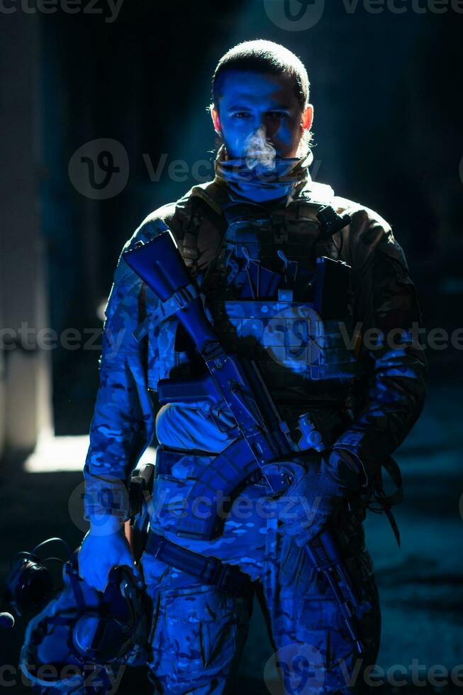 Army soldier in Combat Uniforms with an assault rifle and combat helmet night mission dark background. Blue and purple gel light effect. photo