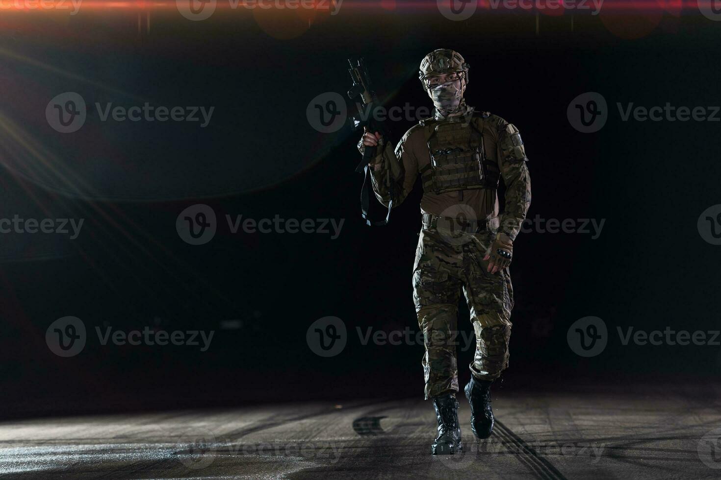 Army soldier in Combat Uniforms with an assault rifle, plate carrier and combat helmet going on a dangerous mission on a rainy night. photo