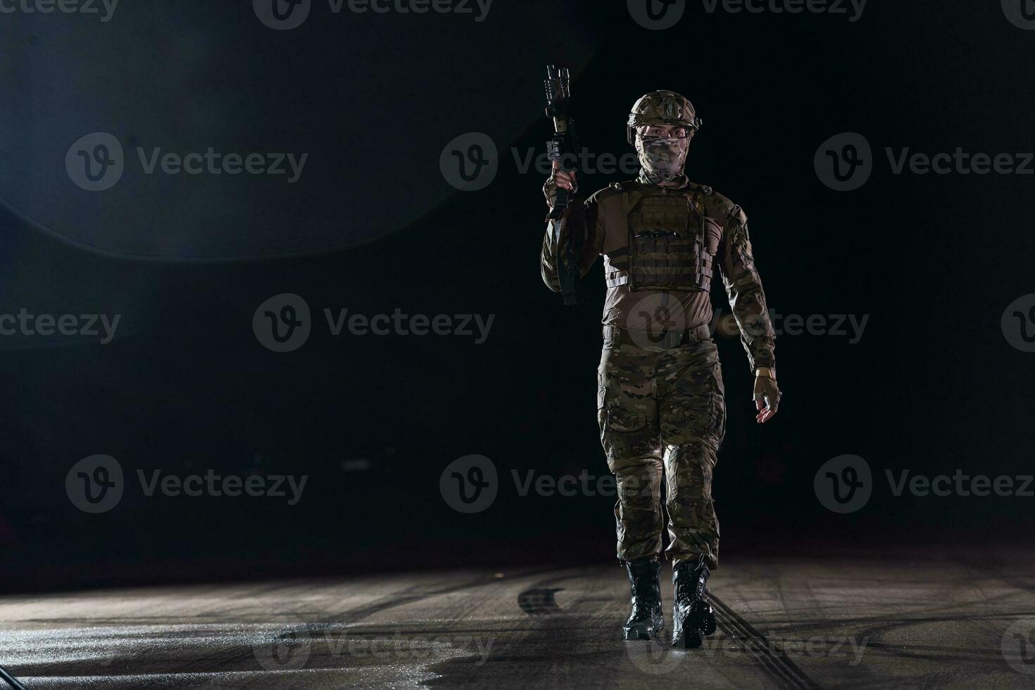 Army soldier in Combat Uniforms with an assault rifle, plate carrier and combat helmet going on a dangerous mission on a rainy night. photo