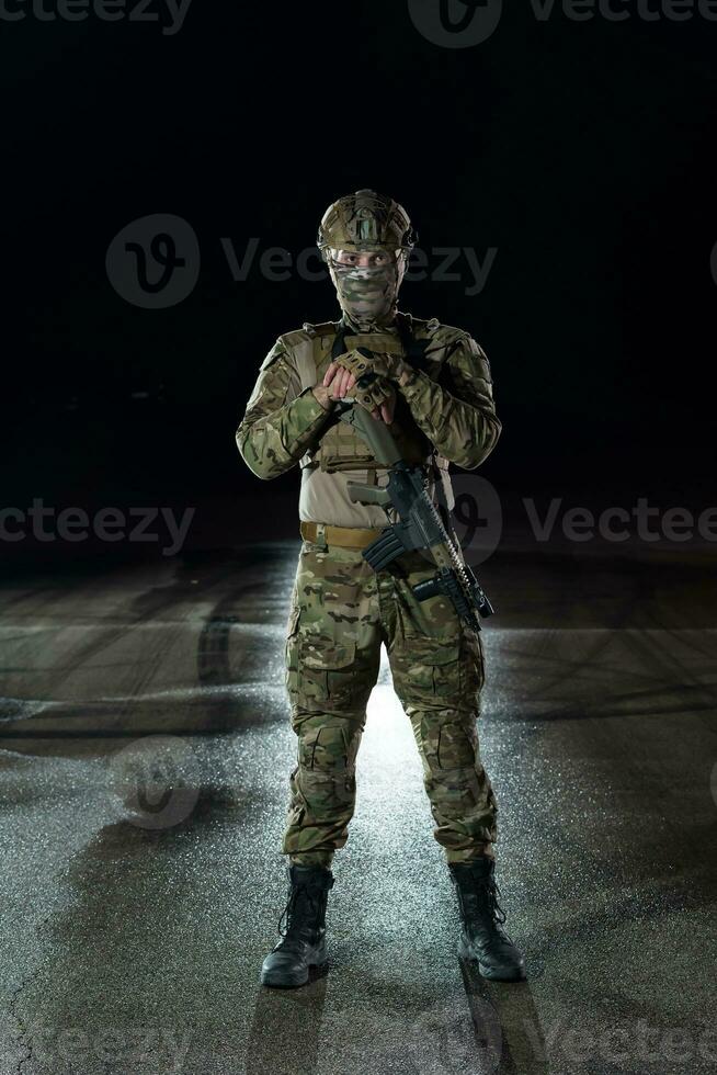 Army soldier in Combat Uniforms with an assault rifle, plate carrier and combat helmet going on a dangerous mission on a rainy night. photo