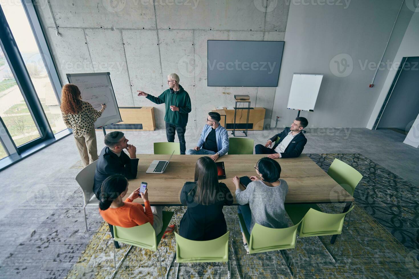 In a modern office setting, a group of business professionals attentively listens to a captivating presentation delivered by their young colleagues, showcasing their teamwork, engagement, and eagerness to learn and grow in a collaborative environment. photo