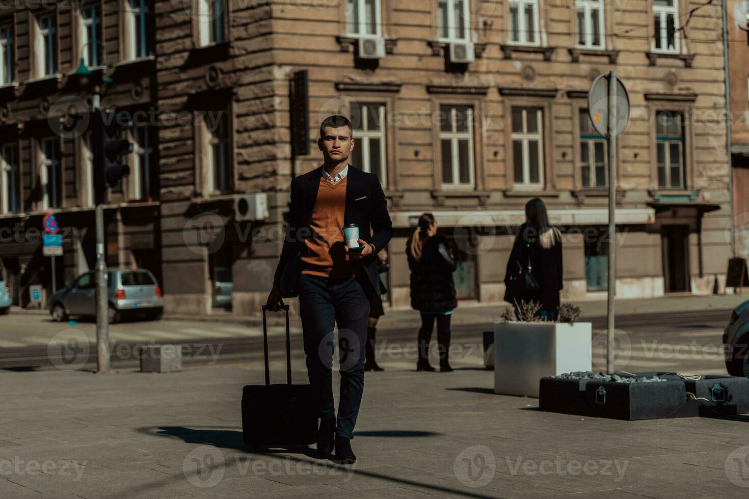 Going to airport terminal. Confident businessman traveler walking on city streets and pulling his suitcase drinking coffee and speaking on smartphone photo