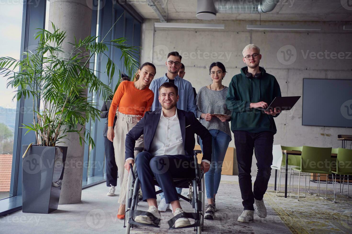 A diverse group of businessmen, including a businessman in wheelchair, confidently stride together through a modern, spacious office, epitomizing collaboration, inclusivity, and strength in unity photo