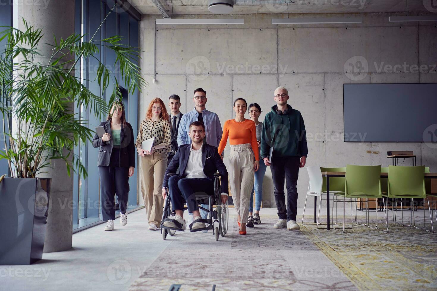 A diverse group of businessmen, including a businessman in wheelchair, confidently stride together through a modern, spacious office, epitomizing collaboration, inclusivity, and strength in unity photo