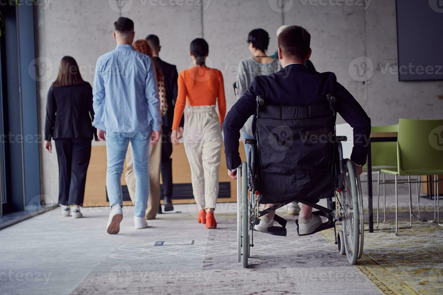 A diverse group of businessmen, including a businessman in wheelchair, confidently stride together through a modern, spacious office, epitomizing collaboration, inclusivity, and strength in unity photo