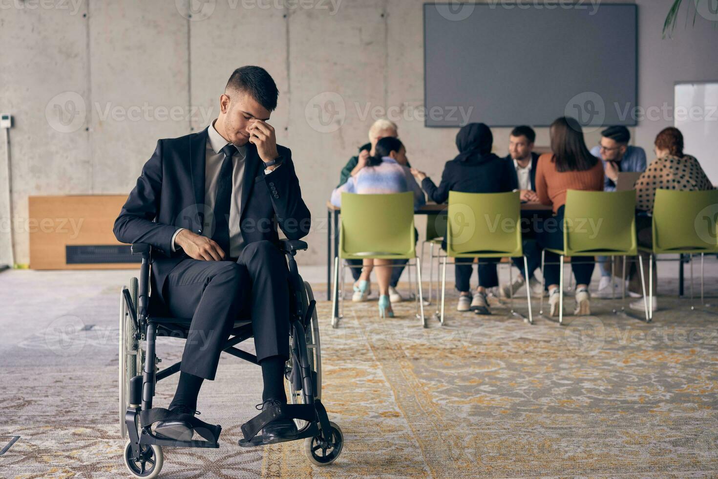 A melancholic businessman in a wheelchair sitting with a sad expression, gazing through the window of a modern office, conveying a sense of solitude photo