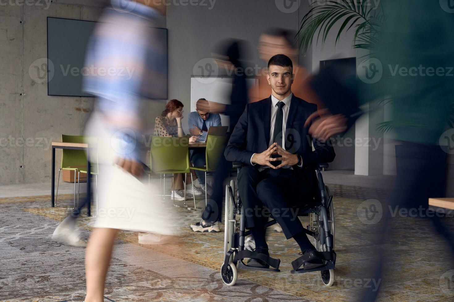 un empresario en un silla de ruedas en un moderno oficina, rodeado por su colegas quien son retratado con borroso movimientos, simbolizando su apoyo y solidaridad como ellos navegar el espacio de trabajo juntos. foto