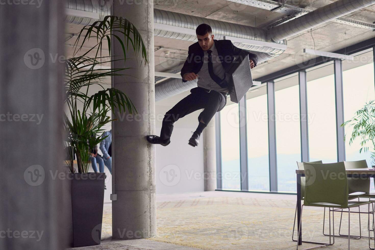 In the modern office, a businessman with a briefcase captivates everyone as he performs thrilling aerial acrobatics, defying gravity with his daring leaps and showcasing his agility with breathtaking showmanship. photo