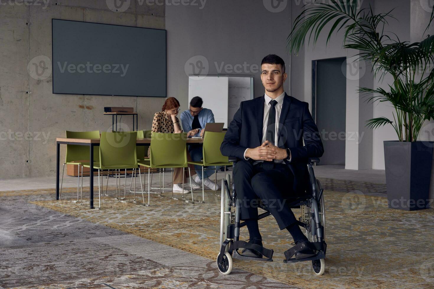 Businessman in a wheelchair commands attention, symbolizing resilience and success amidst a dynamic modern office environment. photo