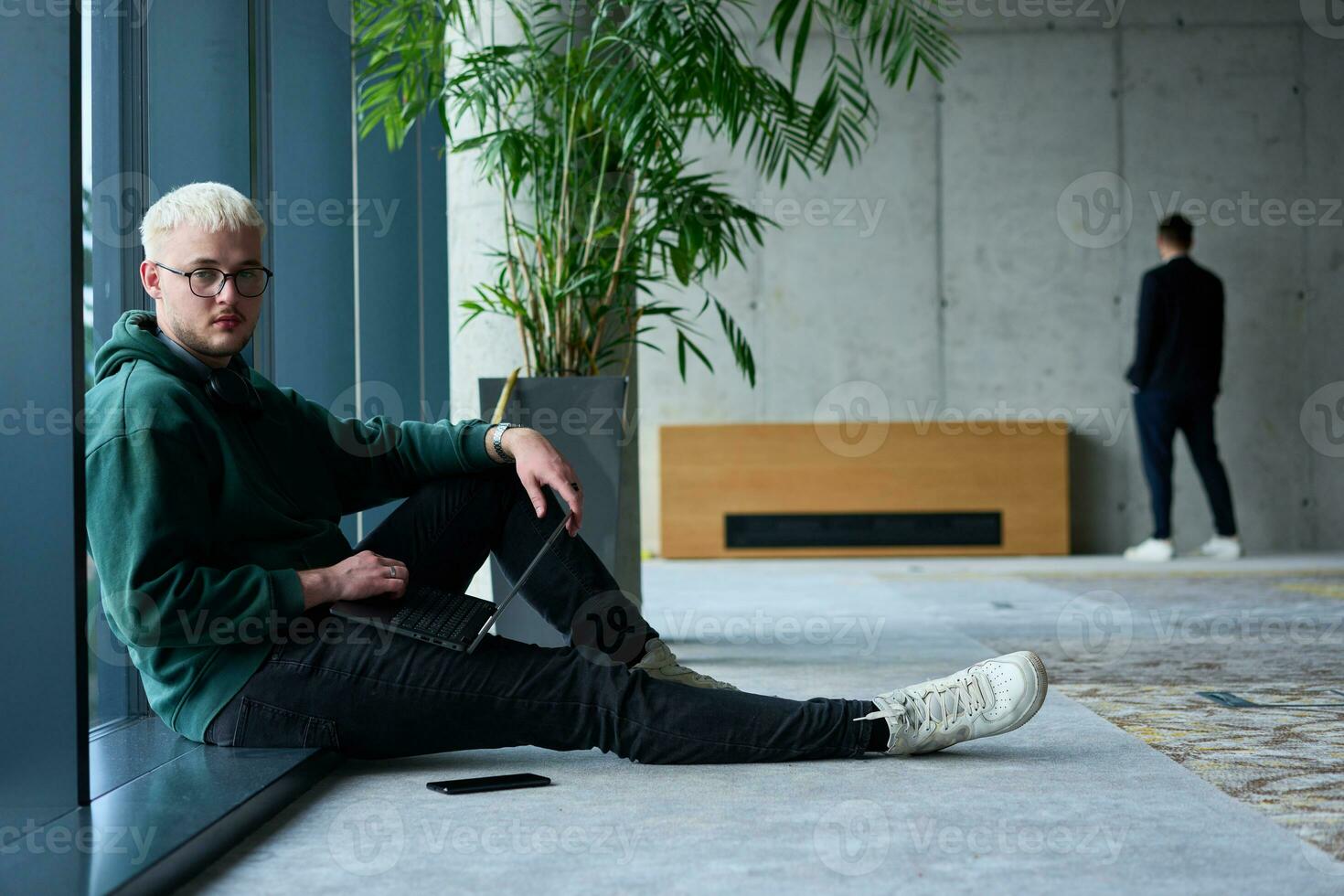 A young blond man in a modern office sits by the window, engrossed in his work on a laptop photo