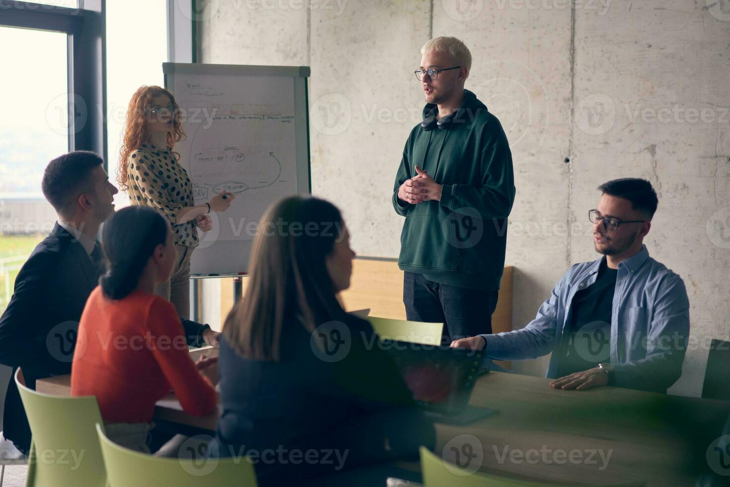 In a modern office setting, a group of business professionals attentively listens to a captivating presentation delivered by their young colleagues, showcasing their teamwork, engagement, and eagerness to learn and grow in a collaborative environment. photo