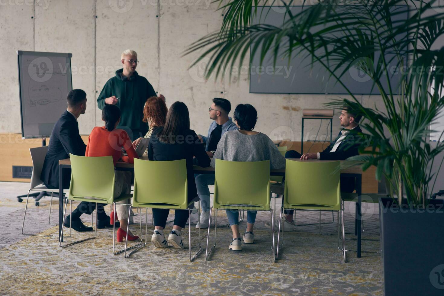 In a modern office setting, a group of business professionals attentively listens to a captivating presentation delivered by their young colleagues, showcasing their teamwork, engagement, and eagerness to learn and grow in a collaborative environment. photo