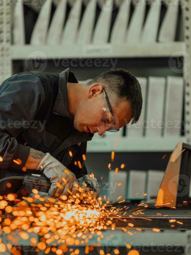 Heavy Industry Engineering Factory Interior with Industrial Worker Using Angle Grinder and Cutting a Metal Tube. Contractor in Safety Uniform and Hard Hat Manufacturing Metal Structures. photo