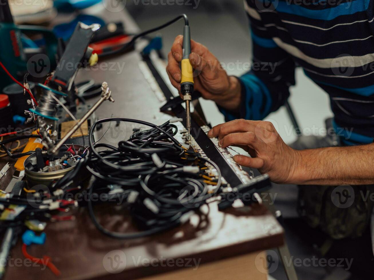 Industrial worker man soldering cables of manufacturing equipment in a factory. Selective focus photo