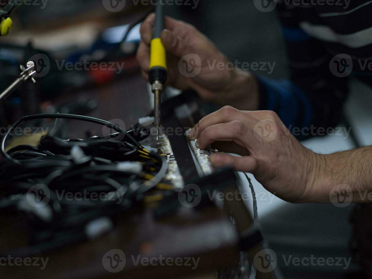 Industrial worker man soldering cables of manufacturing equipment in a factory. Selective focus photo