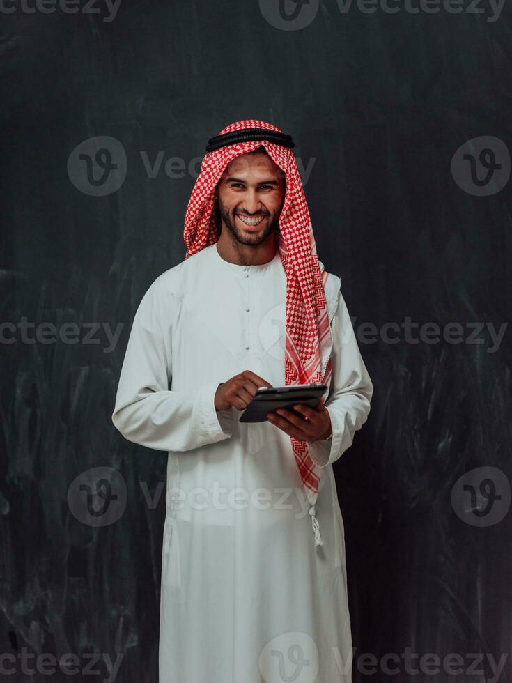 Young arabian muslim businessman using tablet computer wearing hijab clothes in front of black chalkboard photo