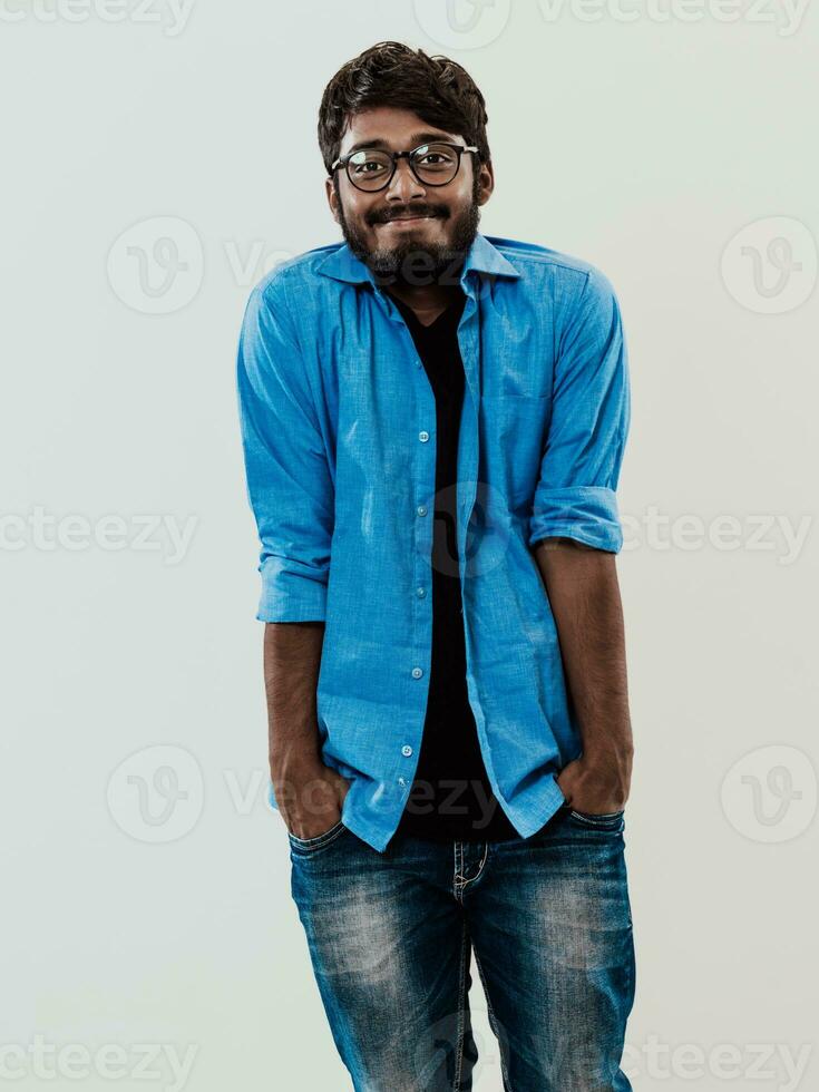 Indian smiling young man with blue shirt and glasses posing on gray background photo