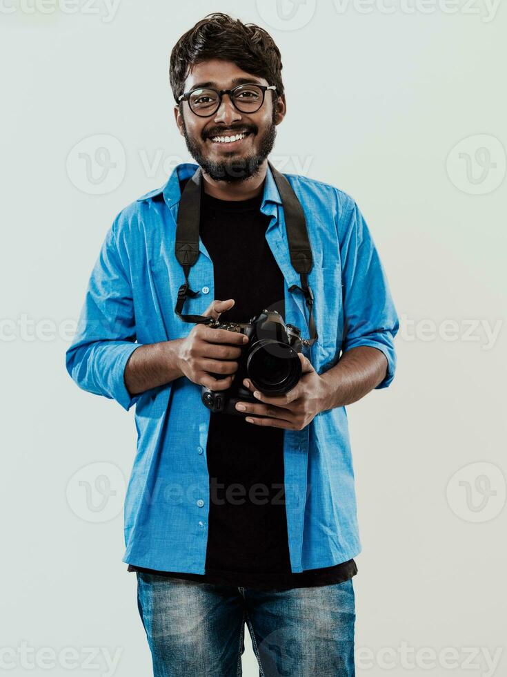 profesional fotógrafo teniendo dslr cámara tomando imagen.indio hombre fotografía entusiasta tomando foto mientras en pie en azul antecedentes. estudio Disparo