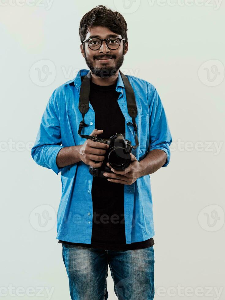 Professional photographer having DSLR camera taking picture.Indian man photography enthusiast taking photo while standing on blue background. Studio shot