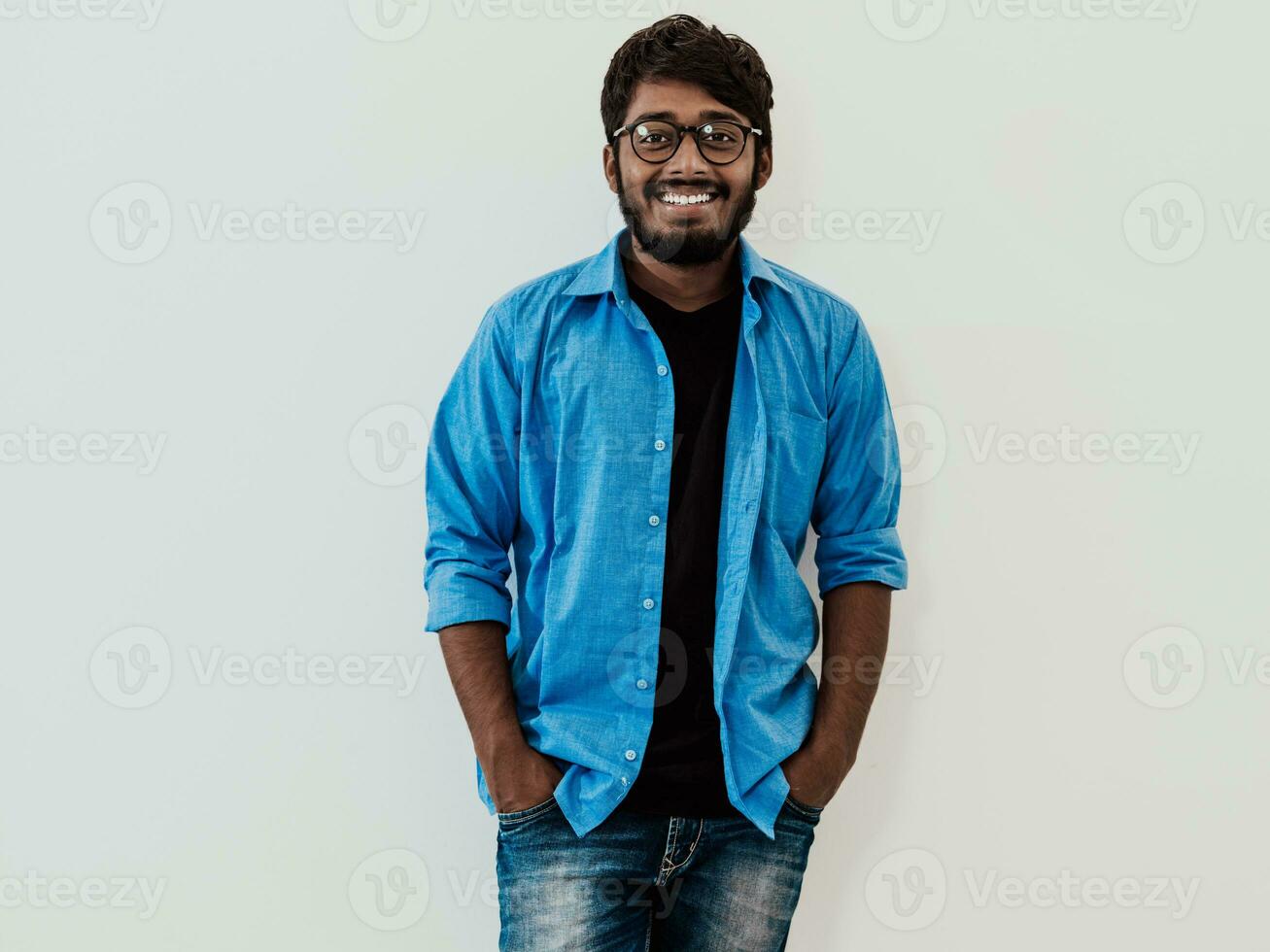 Indian smiling young man with blue shirt and glasses posing on gray background photo