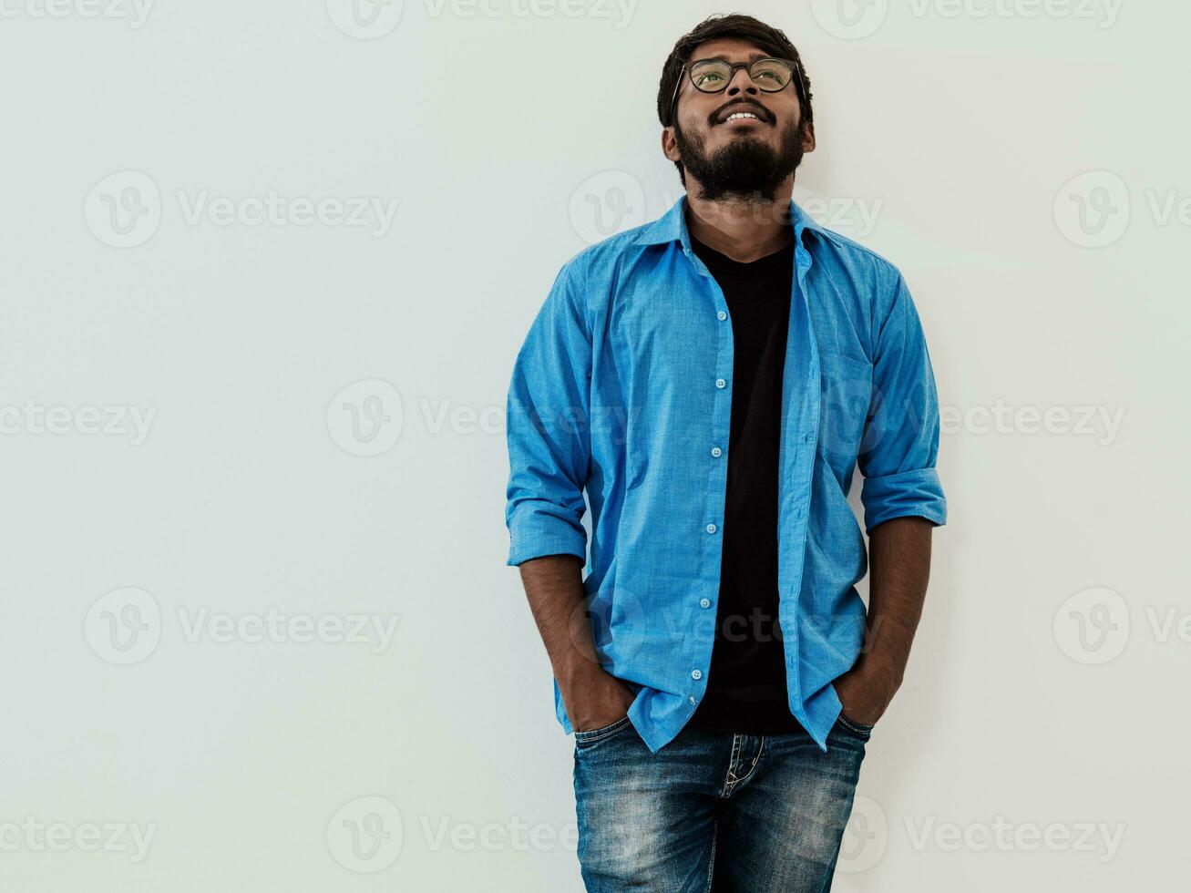 Indian smiling young man with blue shirt and glasses posing on gray background photo